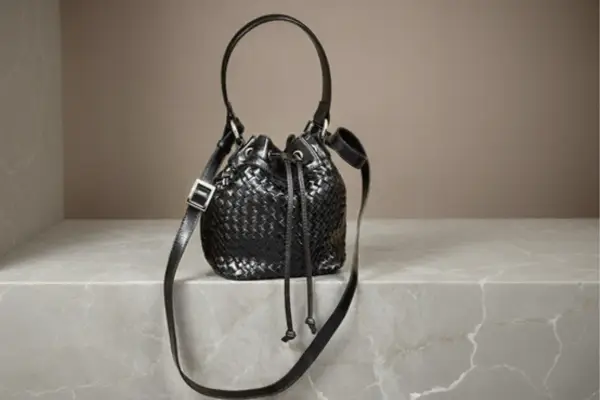 Bolso bucket negro de piel con técnica intrecciato y asa superior, con correa larga ajustable.
